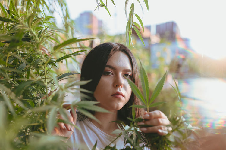 Portrait of young woman holding leaf of cannabis plant