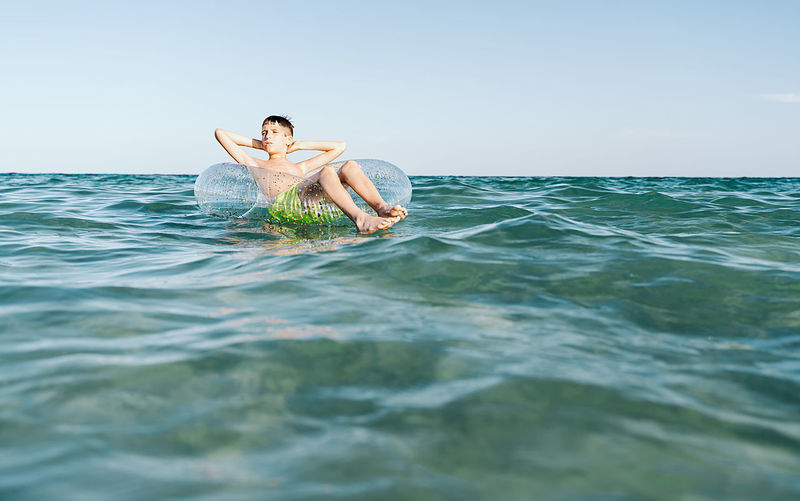 Relaxed white boy swimming in a float in the sea enjoying calm waves in summertime