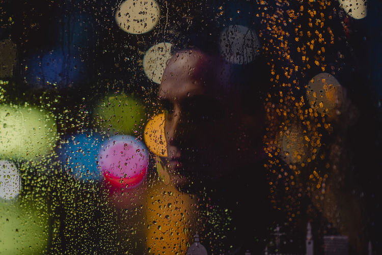 Woman seen through wet glass window during rainy season