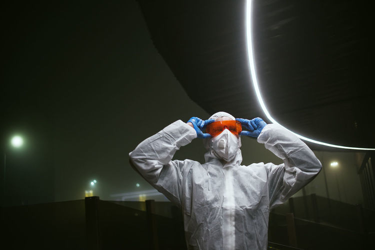 Astronaut holding protective sunglasses against illuminated dark background