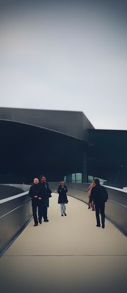 People walking on modern bridge against sky