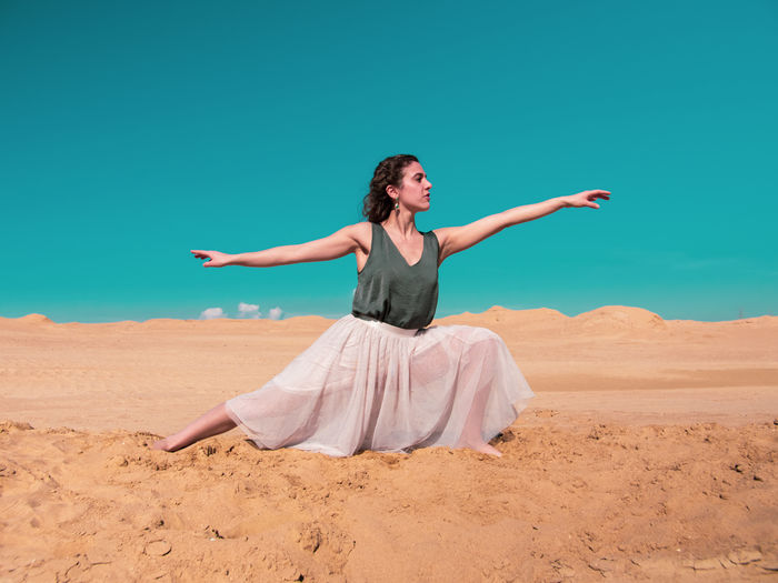 Woman with arms raised on sand against sky