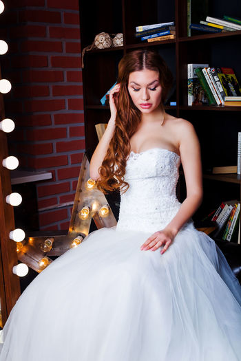 Beautiful bride wearing wedding dress while sitting at home