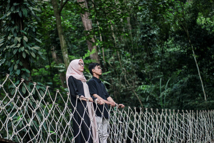 Man and woman on footbridge against trees in forest