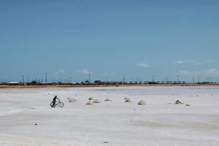 Man with bicycle on salt flat against blue sky