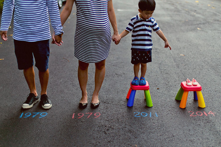 Expectant family of three standing by baby booties with years written on street