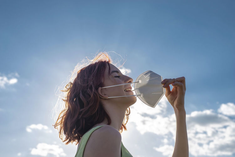 Young woman drinking water against sky