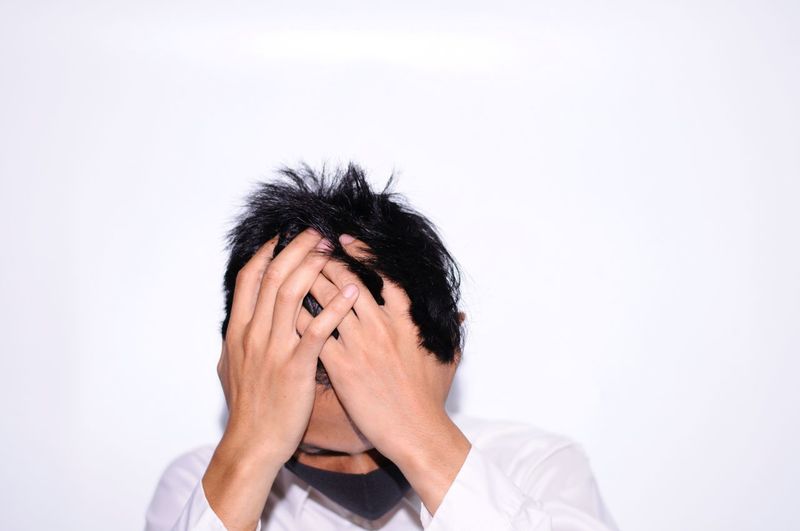 Portrait of man covering face against white background