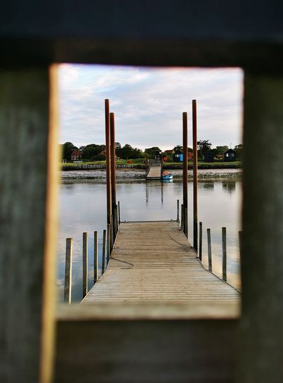 View of jetty and sea looking through hole in fence against sky