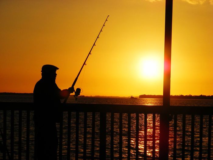 Silhouette man fishing on sea against sunset sky