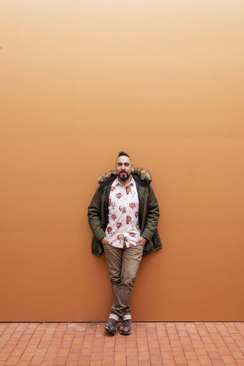 Portrait of young man standing against orange wall