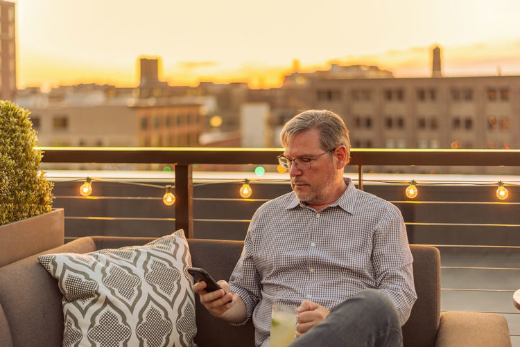 Mature man using phone at terrace during sunset