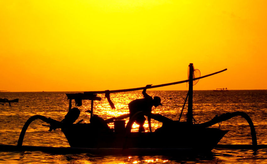 Silhouette man on boat in sea against clear orange sky during sunset