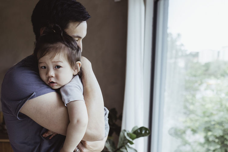 Father carrying baby son by window at home