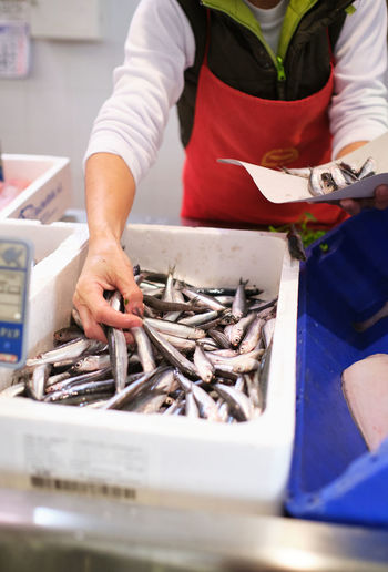 Young woman works in a fish shop, prepares blue fish to sell to her cu
