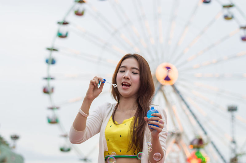 Young woman blowing bubbles while standing in amusement park