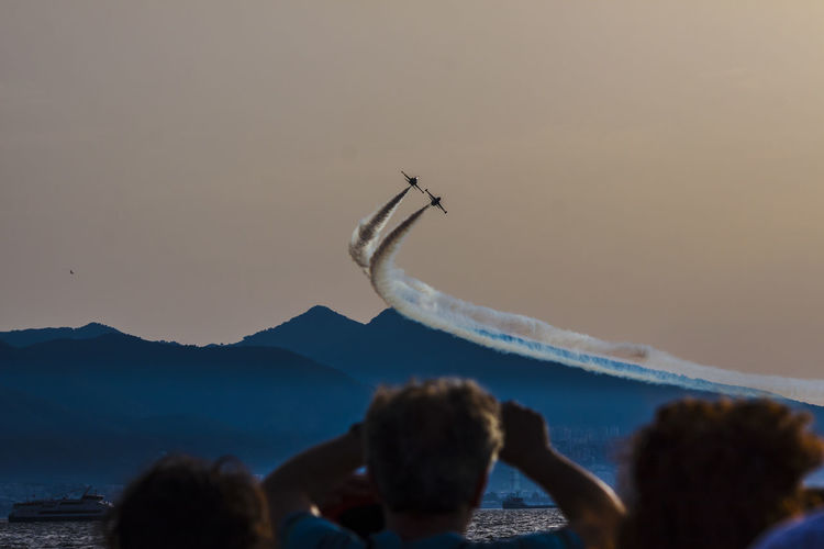 Low angle view of people watching airshow against sky