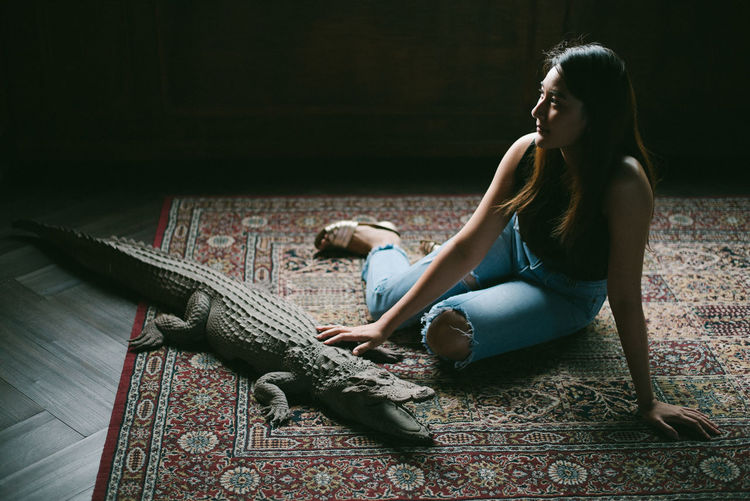 Young woman sitting by crocodile statue on floor