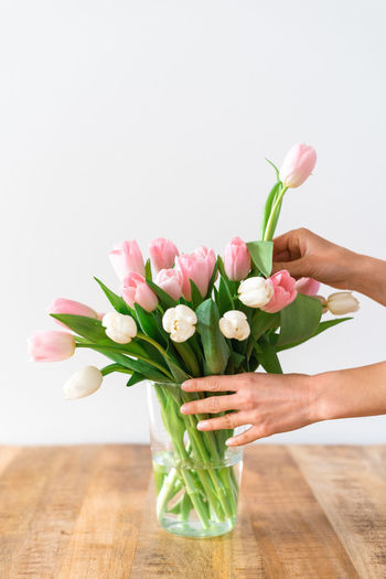 Cropped hands of woman holding flowers on table against white background