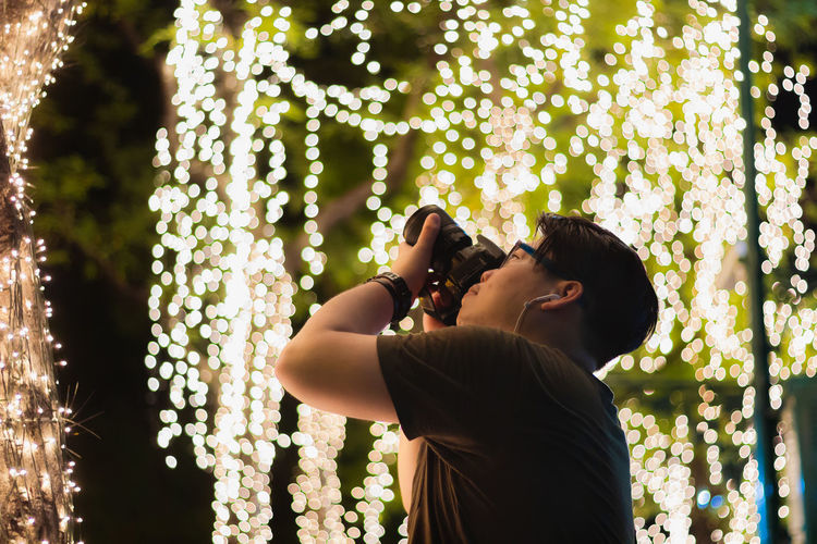 Man photographing through camera against illuminated lights at night