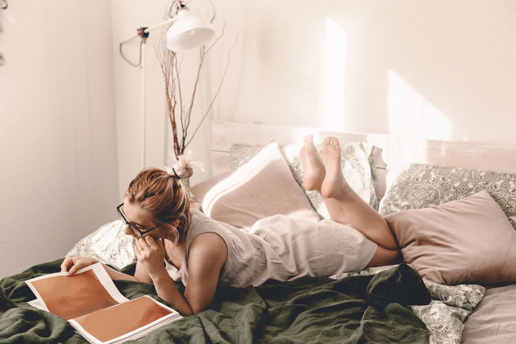 Woman reading book while lying on bed at home