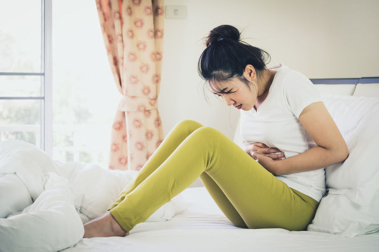 Woman with stomachache sitting on bed