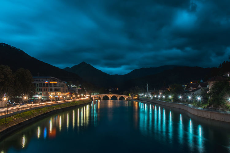 Illuminated bridge over river against sky at night