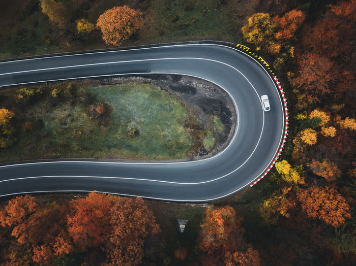 Scenic aerial view of rural curved road with white car in colorful autumn forest.