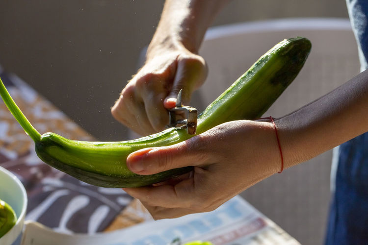 Female hands peeling cucumber in the kitchen.
