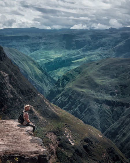 Man sitting on mountain against cloudy sky