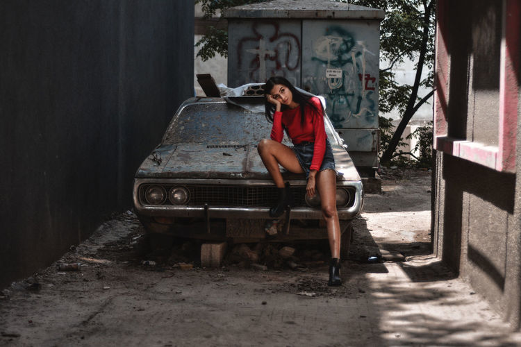 Full length of woman sitting on abandoned car