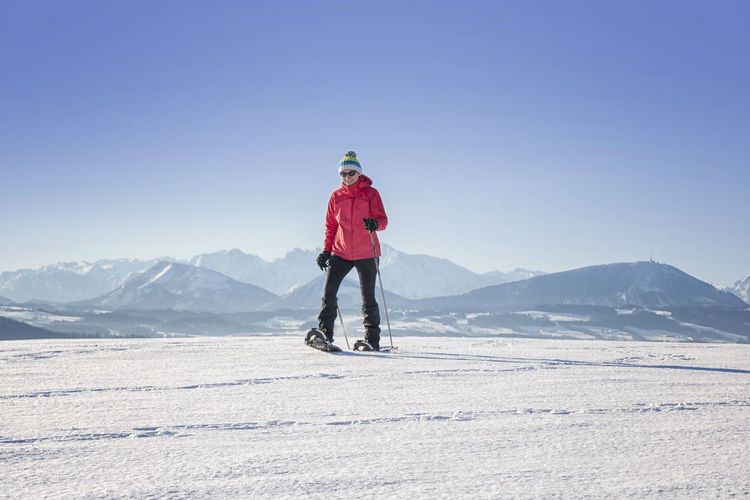 Woman snowboarding on land against clear blue sky
