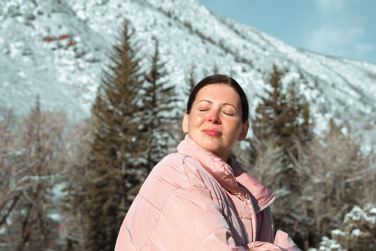 Outdoor portrait of happy woman traveler in winter clothes on snowy mountains background. 