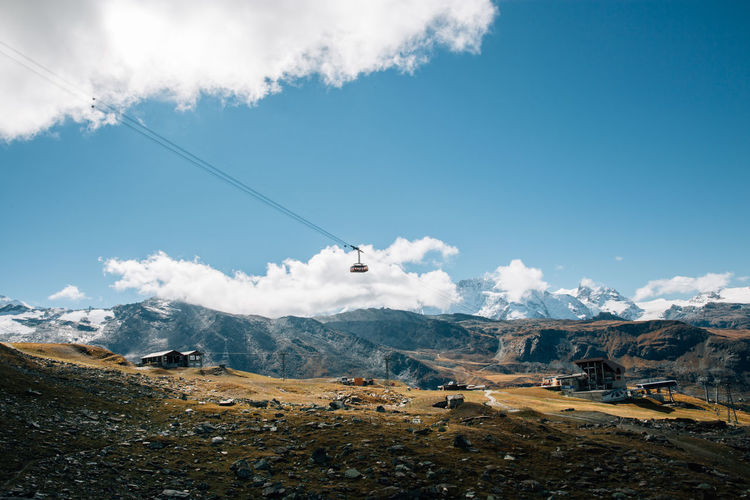 Low angle view of overhead cable car over mountains against sky