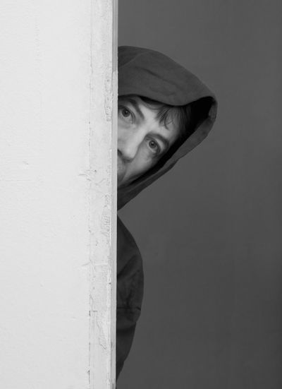 Portrait of man wearing hooded shirt peeking through wall
