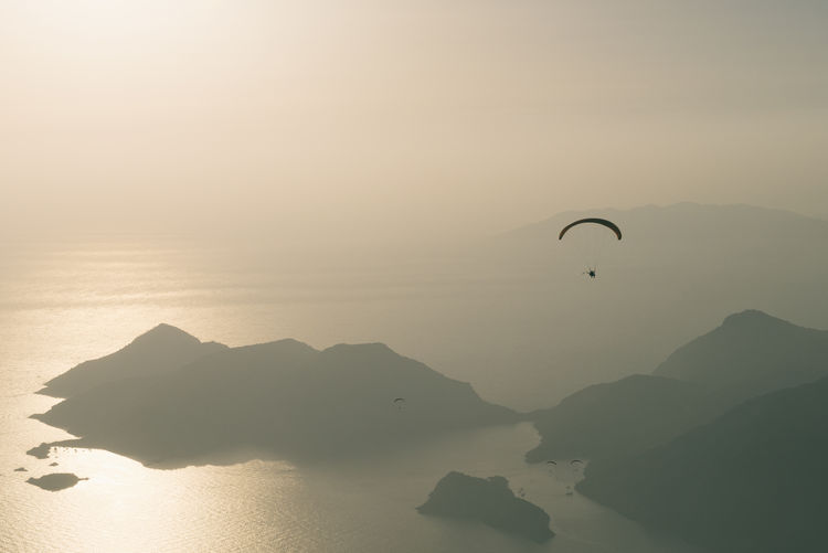 Silhouette person paragliding over sea during sunset