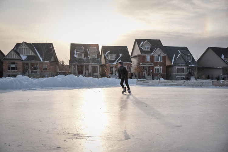 Teenage boy skating alone on a backlit outdoor neighbourhood ice rink.