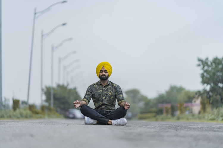 Man in lotus position sitting on road against sky