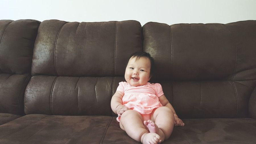 Portrait of smiling baby girl sitting on sofa at home