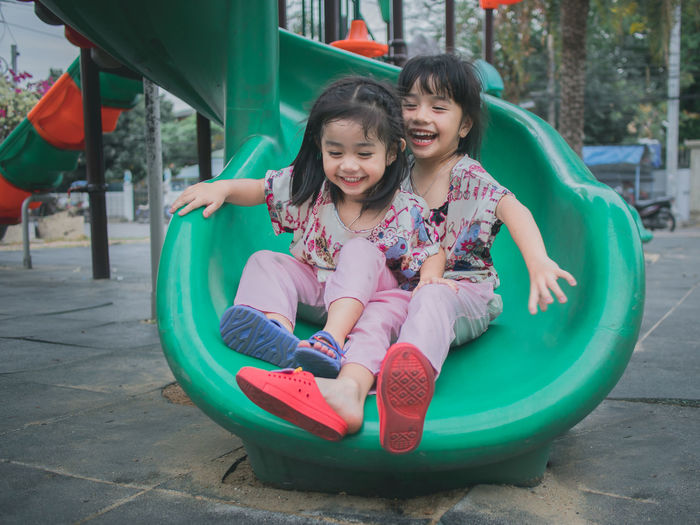 Full length of happy sisters sliding in playground