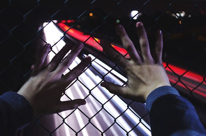 Cropped image of hands on chainlink fence against illuminated light trails