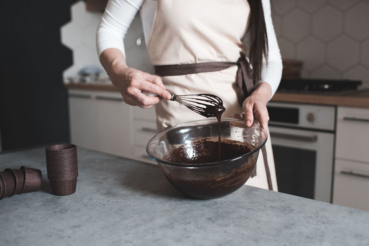 Woman making chocolate batter on table for cupcakes standing in kitchen close up. selective focus.