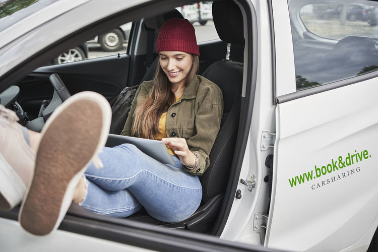 Smiling young woman using digital tablet while sitting in car