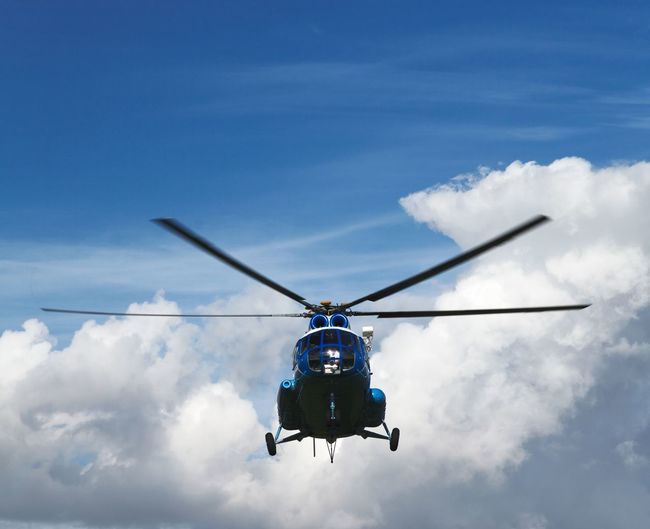 Low angle view of helicopter flying in cloudy sky