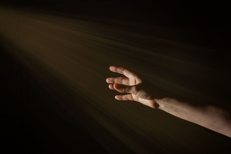 Bright light rays shihing on man's hand in darkness