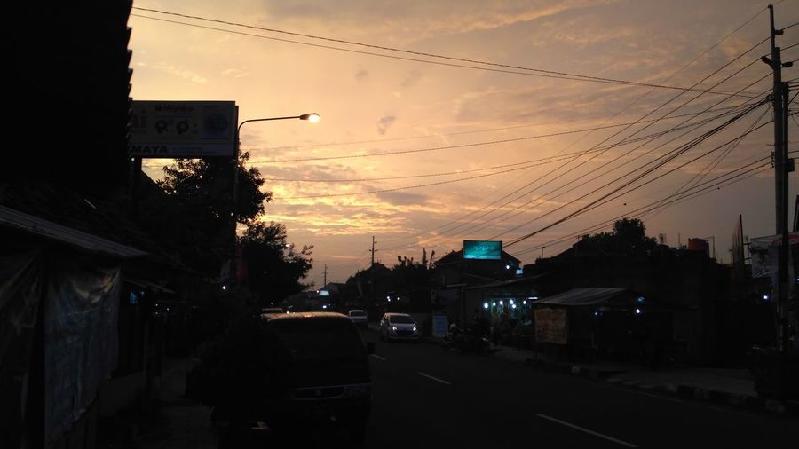 Cars on road amidst buildings against sky during sunset