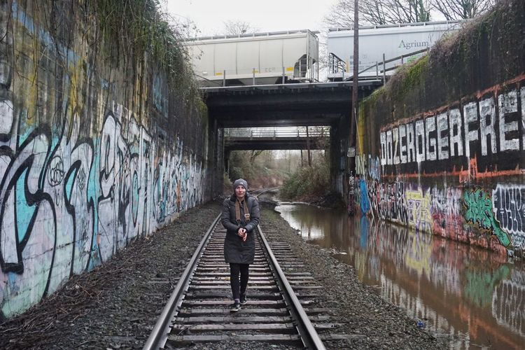 Woman standing on railroad tracks near graffiti walls