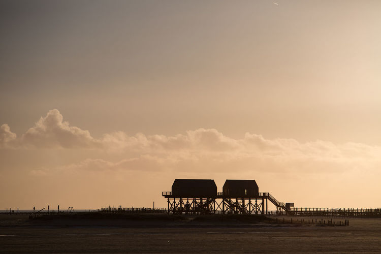 Silhouette built structure by sea against sky during sunset