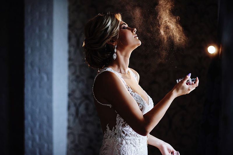 Side view of female model spraying perfume in darkroom