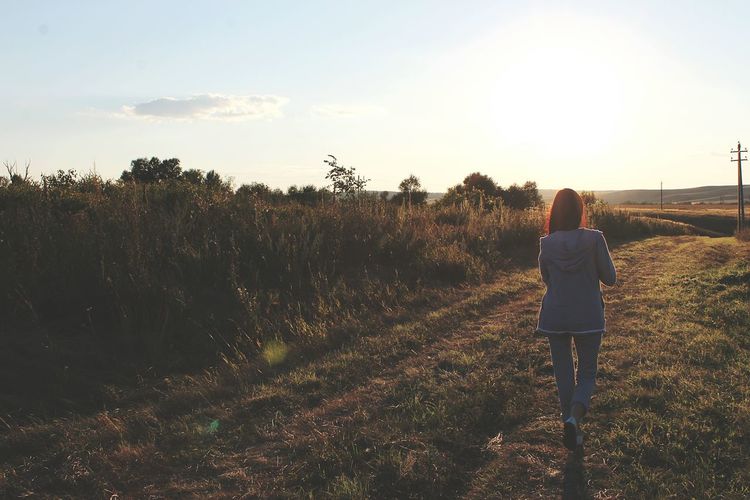 Rear view of woman walking on field against sky